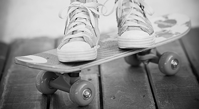 Pieds en espadrilles sur une planche à roulettes posée sur un balcon de bois (noir et blanc)