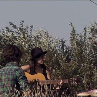 Trois jeunes adultes jouent de la musique en plein air avec des guitares et un violoncelle.