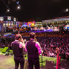 Scène extérieure lors d'un festival. Sur la scène, il y a un chanteur, un trompettiste et un saxophoniste.