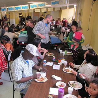 Des nouveaux arrivants sont rassemblés dans une salle de réception pour partager un repas collectif.