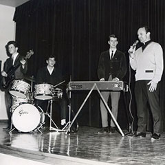 Un groupe de musiciens (chanteur, guitariste, bassiste, claviériste et batteur) se produit sur une scène.