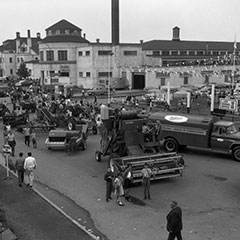 Des machines agricoles sont exposées devant les bâtiments du Colisée de Trois-Rivières. Des gens circulent entre les machines.
