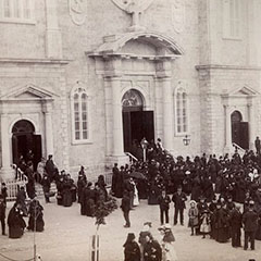 Des gens sortent de l'église de Sainte-Anne-de-Beaupré vêtus de leurs beaux habits. Plusieurs personnes discutent en groupes.